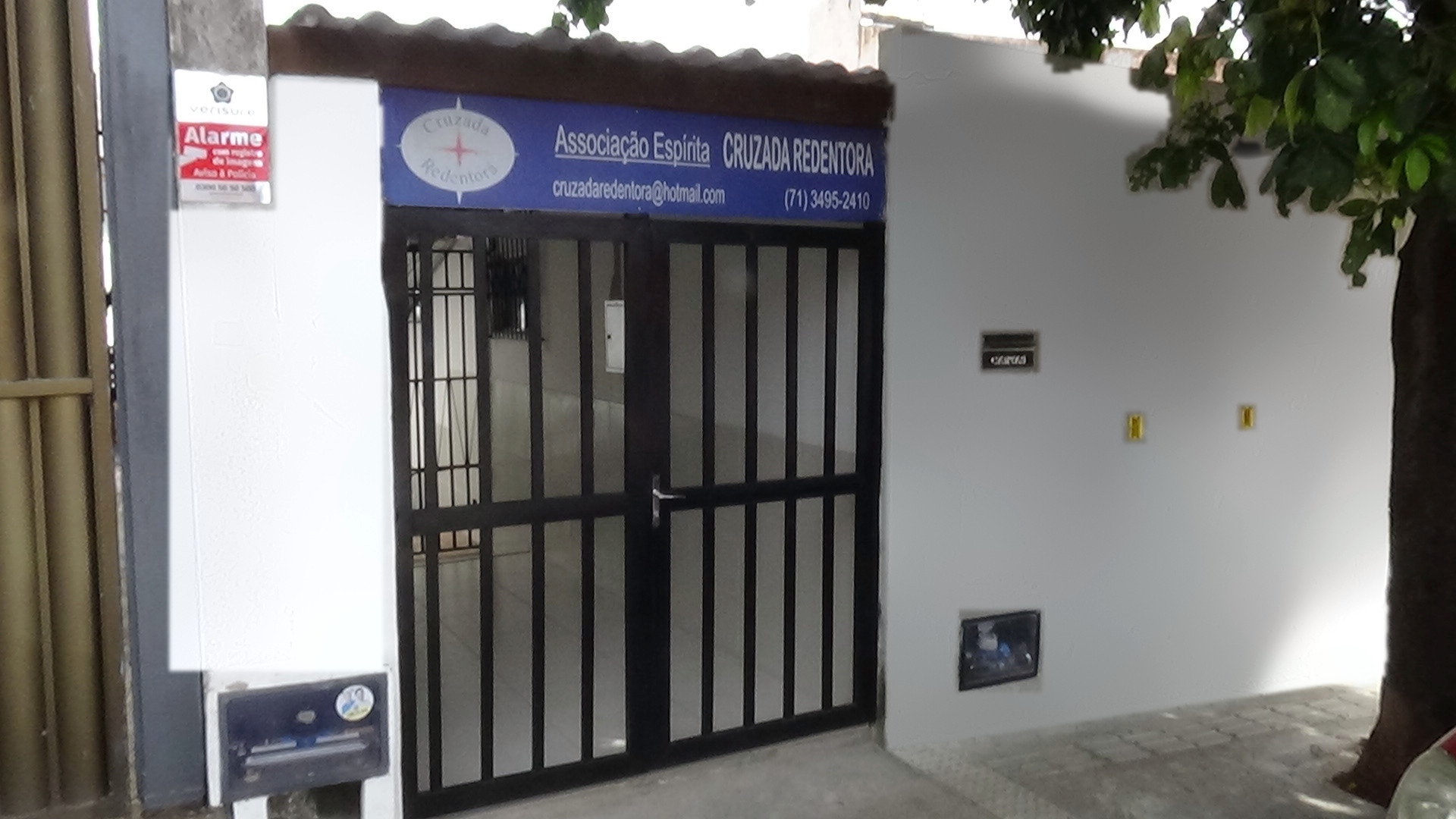 Fachada da Cruzada Redentora: muro branco com detalhes azuis, portão escuro e a placa azul da Associação Espírita